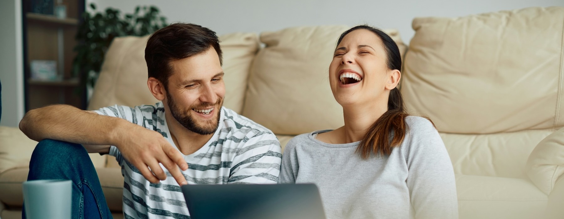 a couple sitting on the ground laughing with a laptop